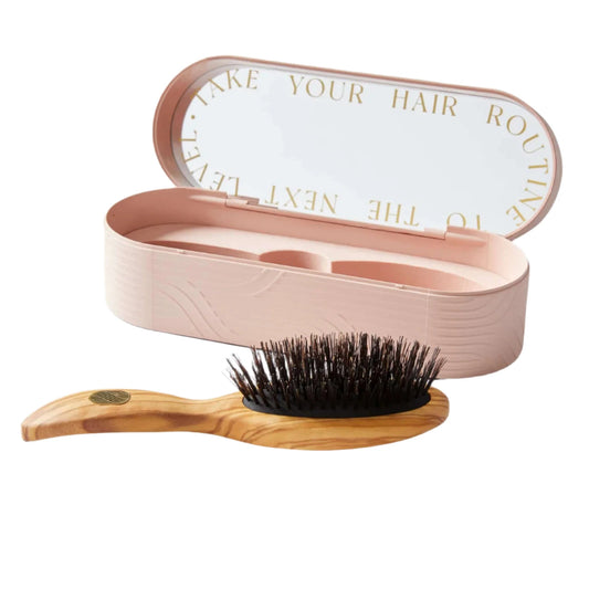A pink hairbrush with boar bristles is displayed next to its open case, which has a capacity for storing the brush and additional compartments for hair accessories.