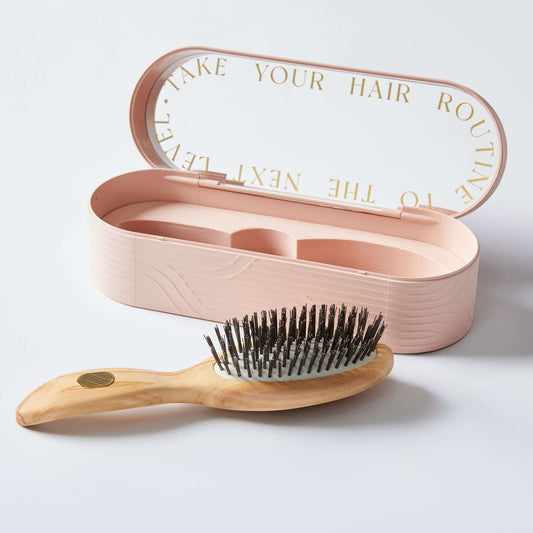 A pink gentle detangling hairbrush with a wooden handle, displayed next to its matching pink case with text on the inside lid.