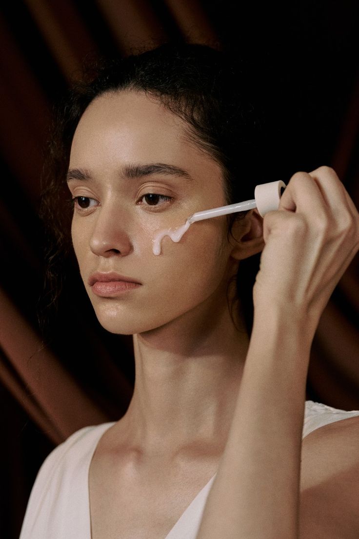 Woman applying skincare product with a dropper against a dark background.