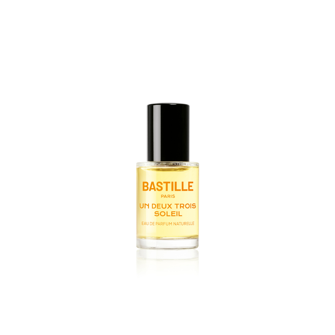 A bottle of 'Un Deux Trois Soleil EDP' by Bastille, with a brown cardboard packaging behind it. The bottle has a black cap and the brand name is displayed prominently on the front.