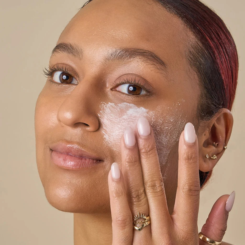 Woman applying cream to her face with a neutral background