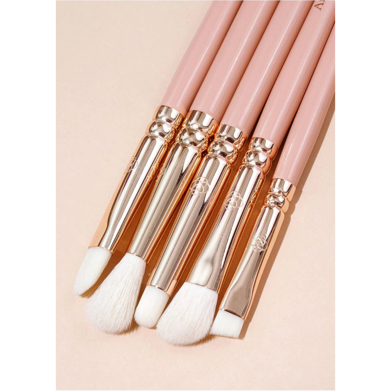 Set of makeup brushes with pink handles and gold accents on a beige background