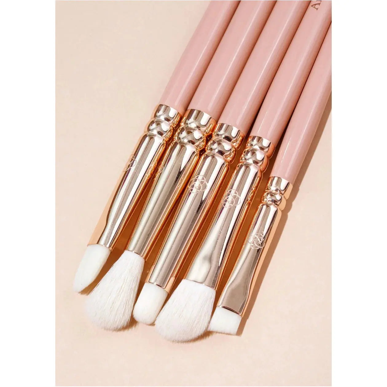 Set of makeup brushes with pink handles and gold accents on a beige background