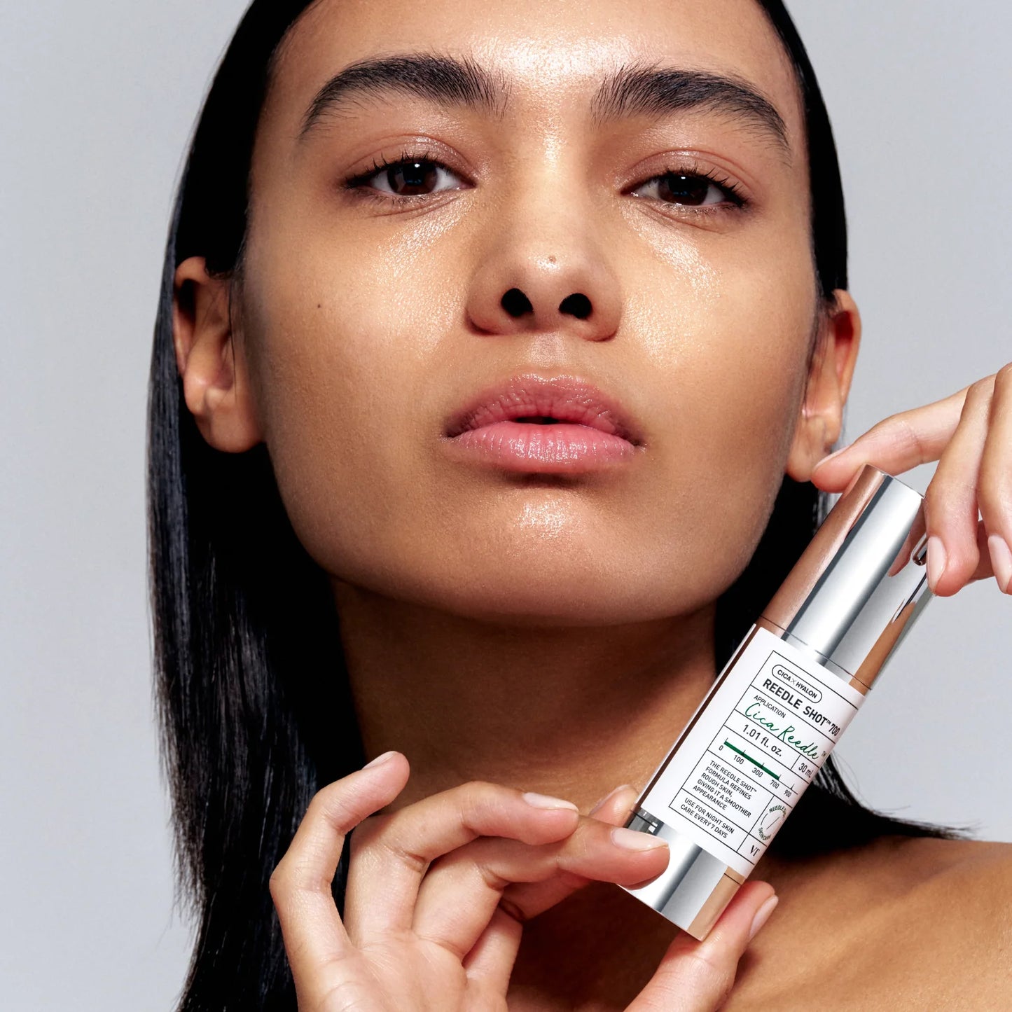 Woman holding a skincare product against a neutral background