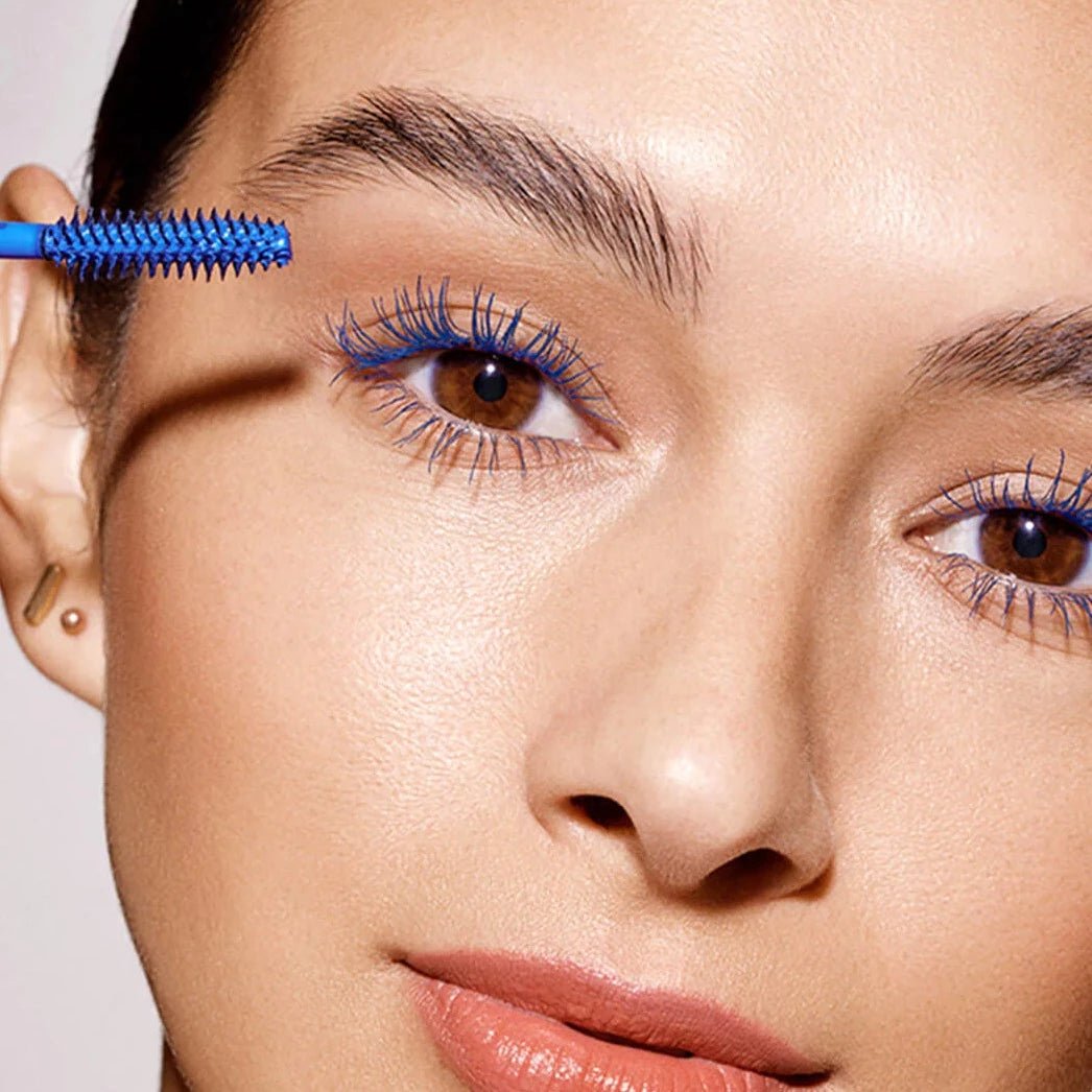 Close-up of a woman applying blue mascara to her eyelashes with a brush.