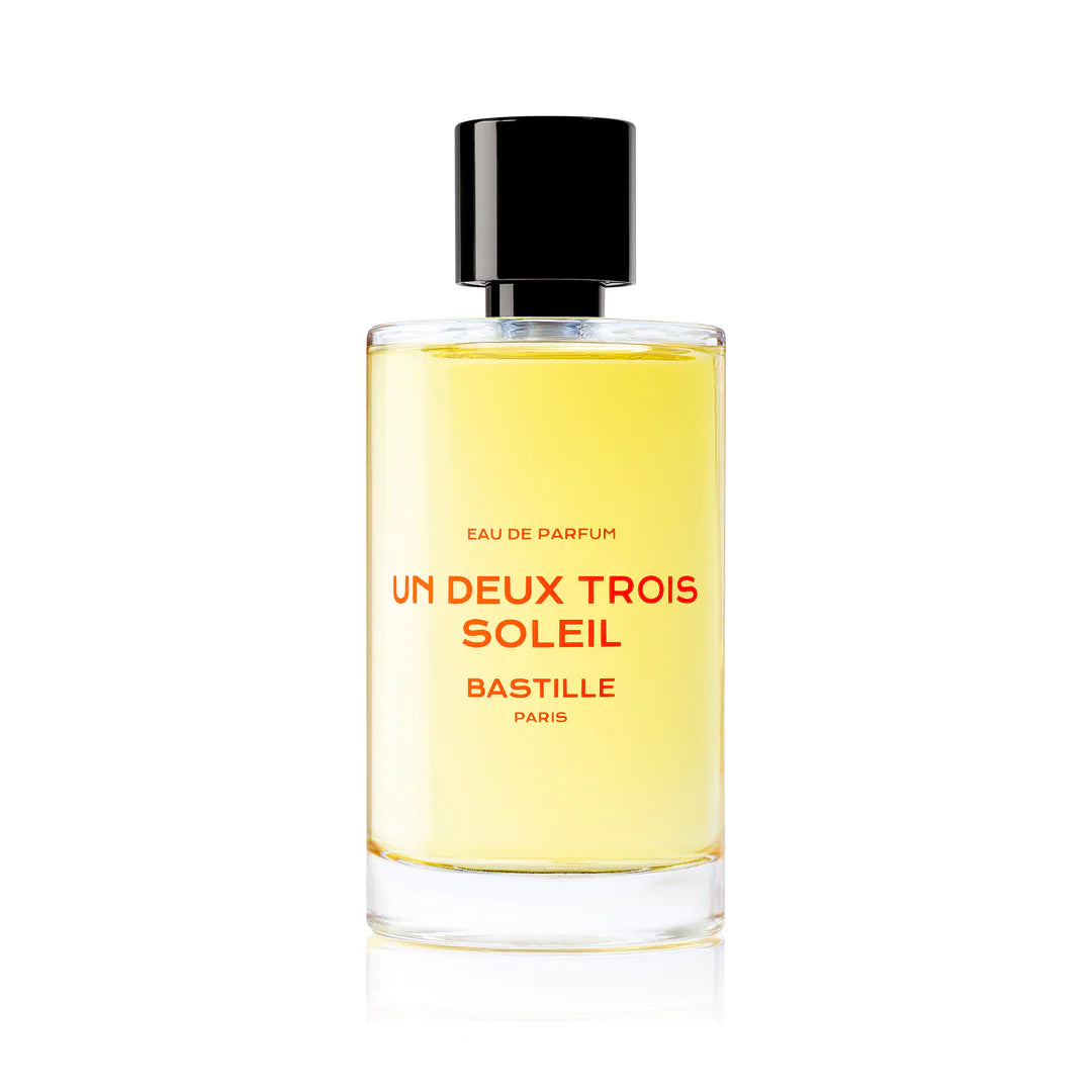 A bottle of 'Un Deux Trois Soleil EDP' by Bastille, with a brown cardboard packaging behind it. The bottle has a black cap and the brand name is displayed prominently on the front.