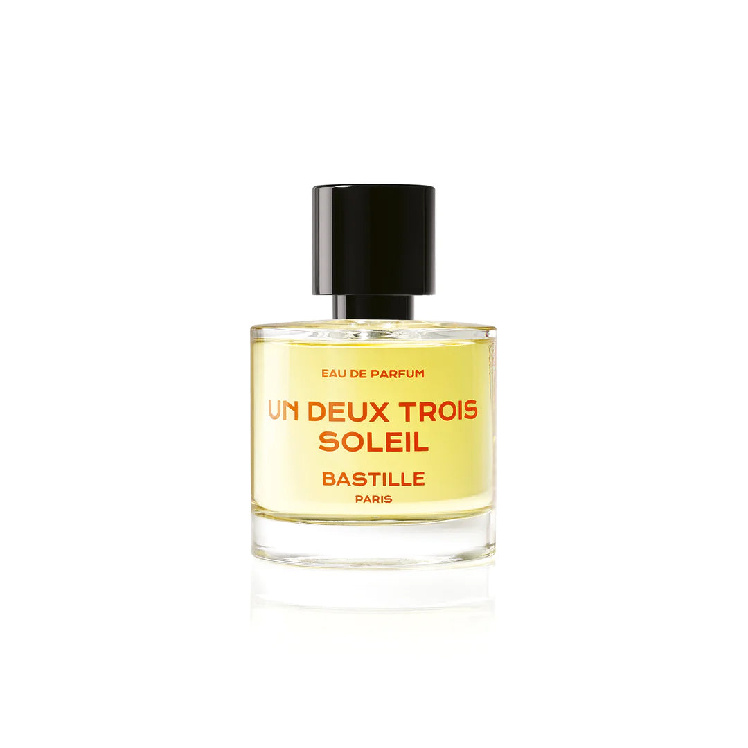 A bottle of 'Un Deux Trois Soleil EDP' by Bastille, with a brown cardboard packaging behind it. The bottle has a black cap and the brand name is displayed prominently on the front.