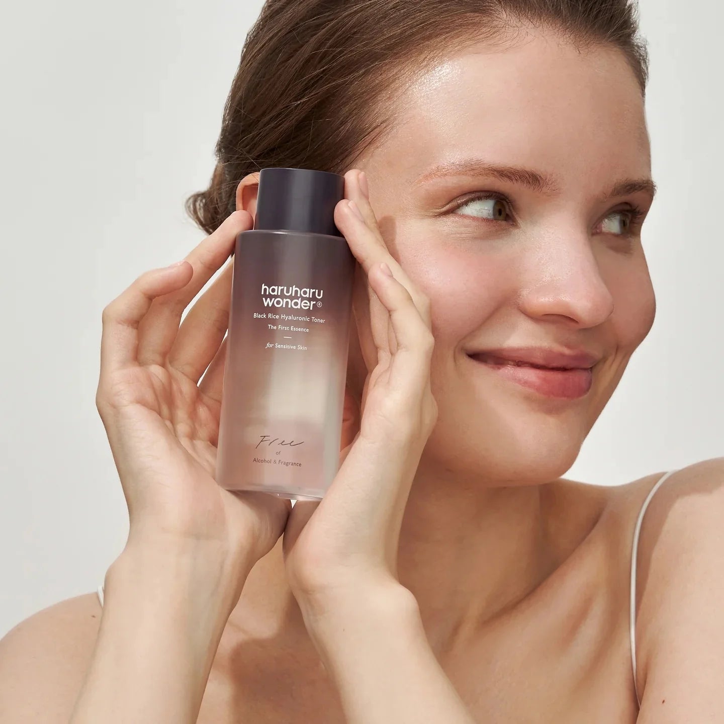 Woman holding a skincare product labeled 'haruharu wonder' against a plain background