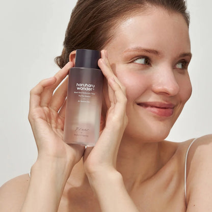 Woman holding a skincare product labeled 'haruharu wonder' against a plain background