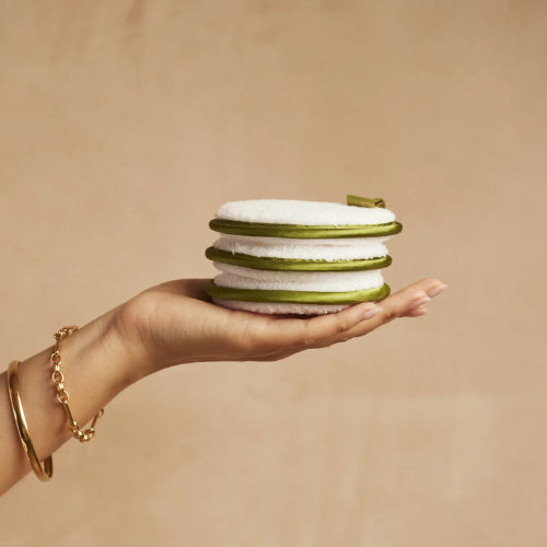 Hand holding a stack of green and white layered items against a beige background