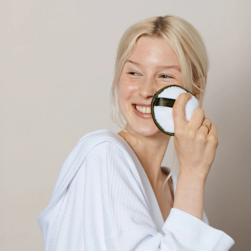 Woman in a white robe holding a round mirror with a black border.