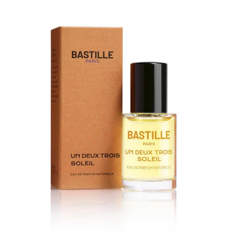 A bottle of 'Un Deux Trois Soleil EDP' by Bastille, with a brown cardboard packaging behind it. The bottle has a black cap and the brand name is displayed prominently on the front.